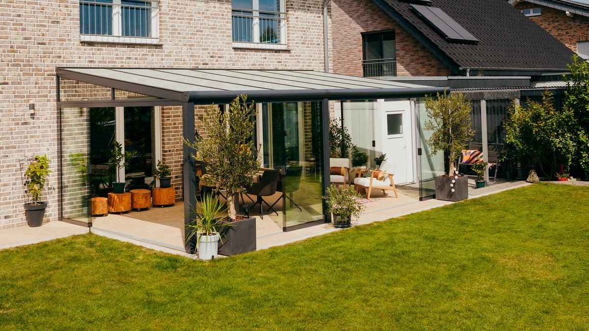 Terrassenüberdachung mit Glasschiebewänden und stimmungsvoller Beleuchtung. Terrassenüberdachung an einem Haus bei Sonnenuntergang.
